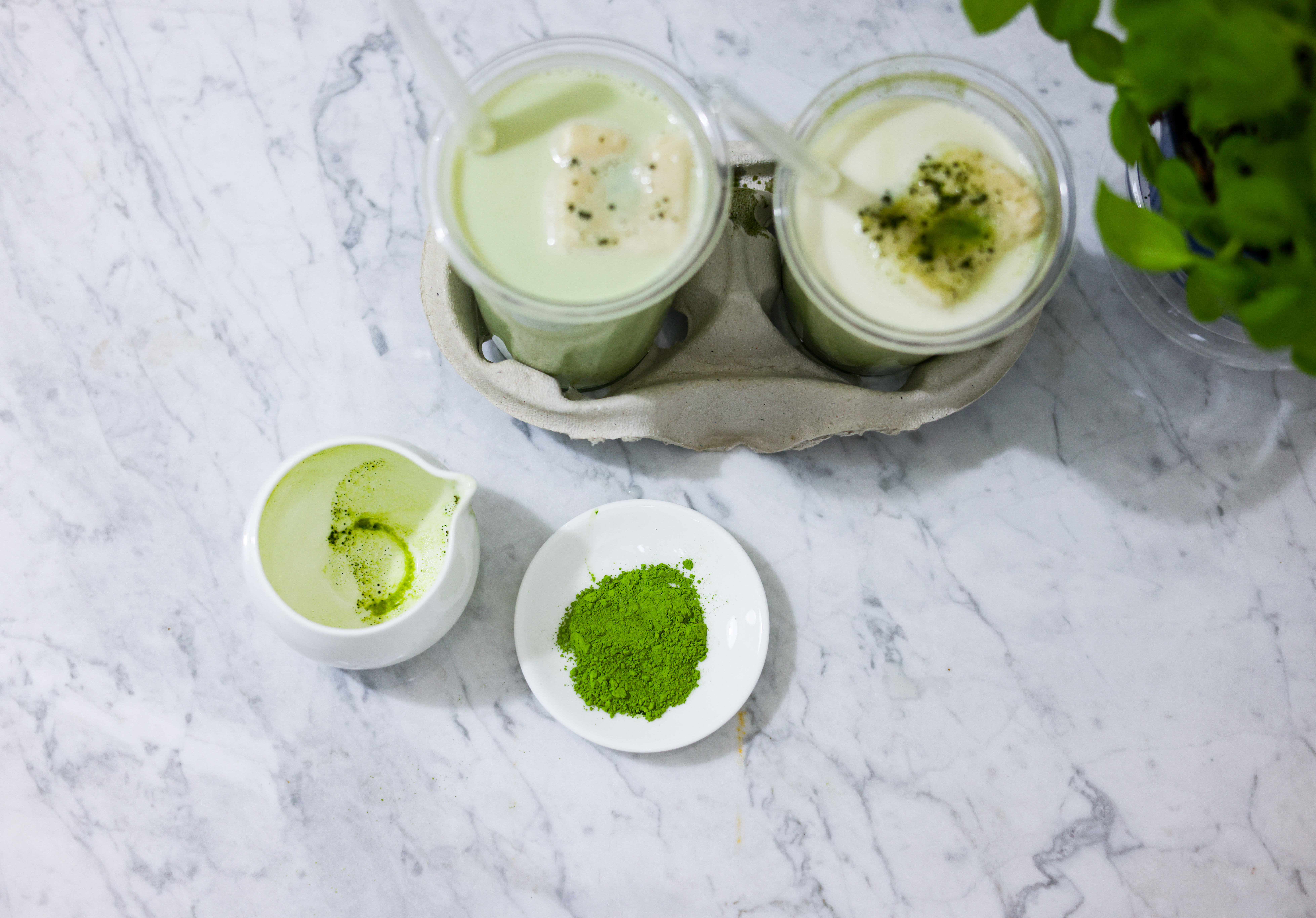 his is a bird's eye view, here you can see both finished Iced Vanilla Matcha cups on the Carrara marble.
In front of them is a porcelain bowl with matcha and the empty porcelain jug I used to pour the matcha into the cups.
Fresh basil can be seen in the background.