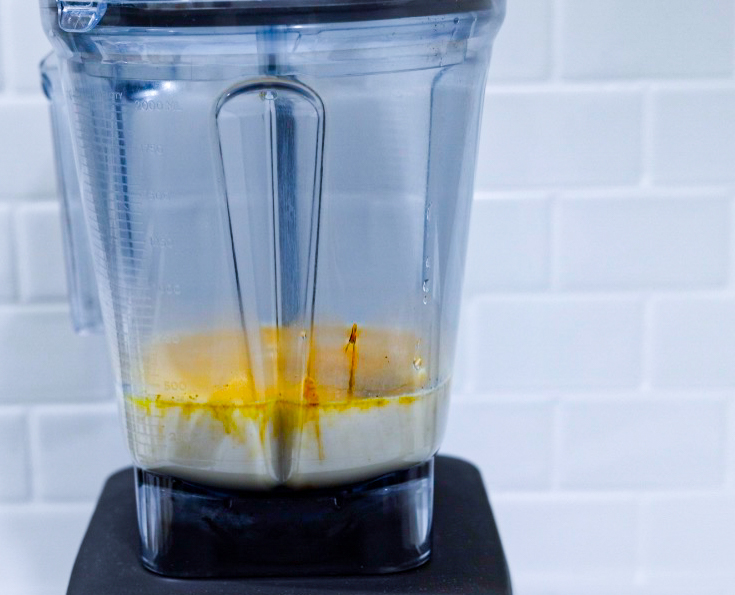 In this picture you can see a vitamix ascent series container filled with oat milk and all turmeric milk Ayurveda ingredients