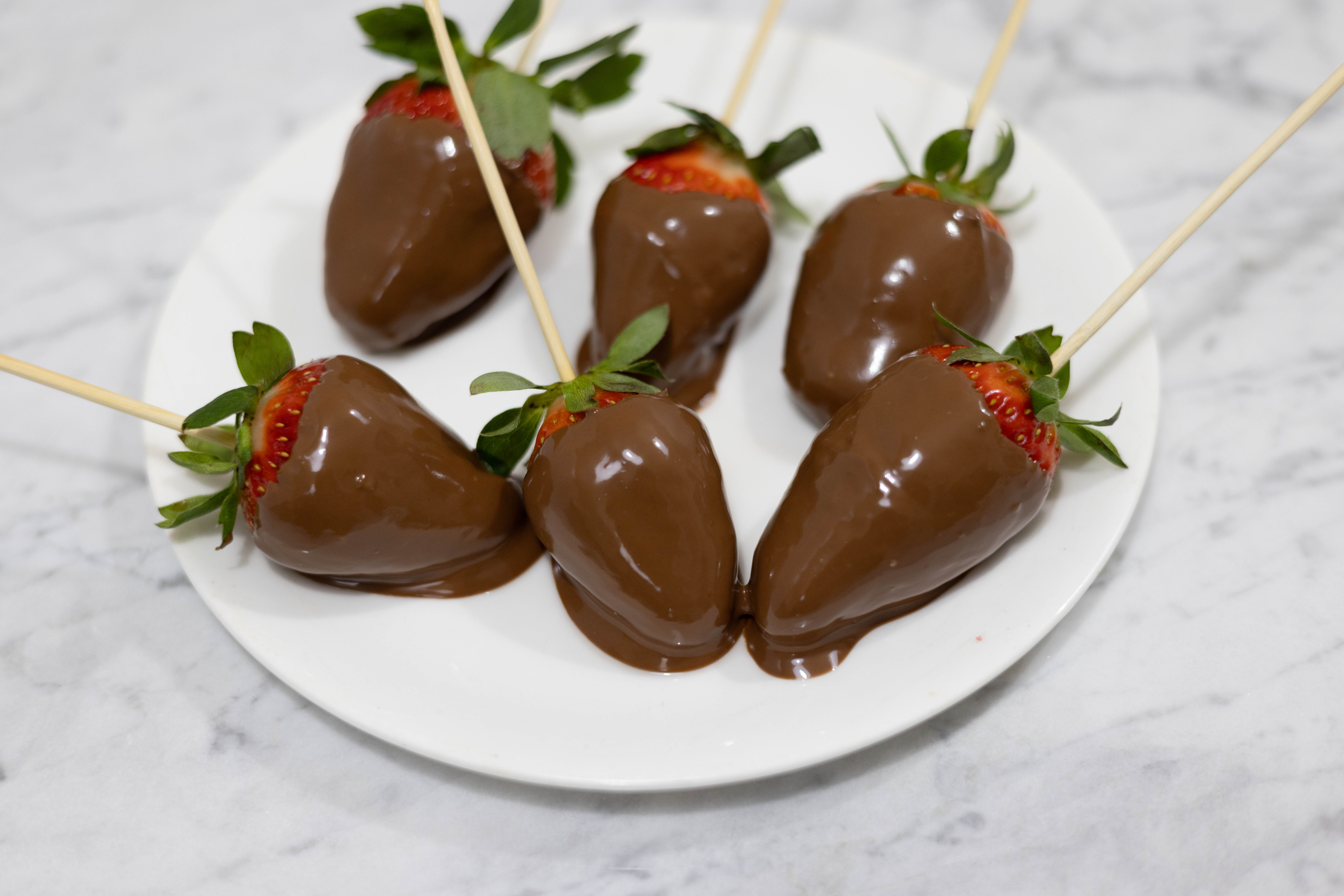 In this picture you can see red organic strawberries with a wood skewer coated with vegan organic chocolate. They are plated on fine bone china porcelain.

The whole setting is positioned on a white Carrara marble desk.
