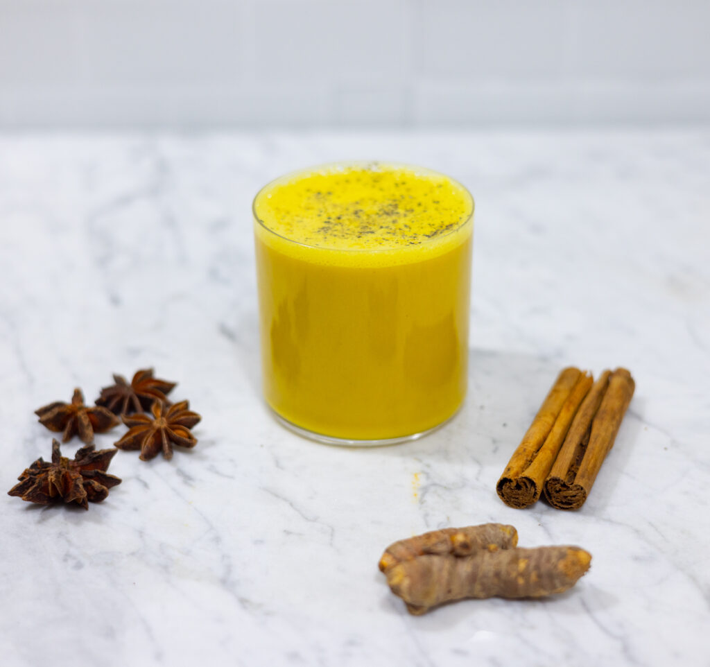 In this picture you can see Turmeric milk Ayurveda. Around this warm beverage you can see spices as, Ceylon cinnamon, star arnis, turmeric. On top of the beverage is organic pepper