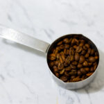 In this picture you can see the barn coffee beans spread on the carrara marble. All objects are placed on white carrara marble and in the back are white metro tiles.