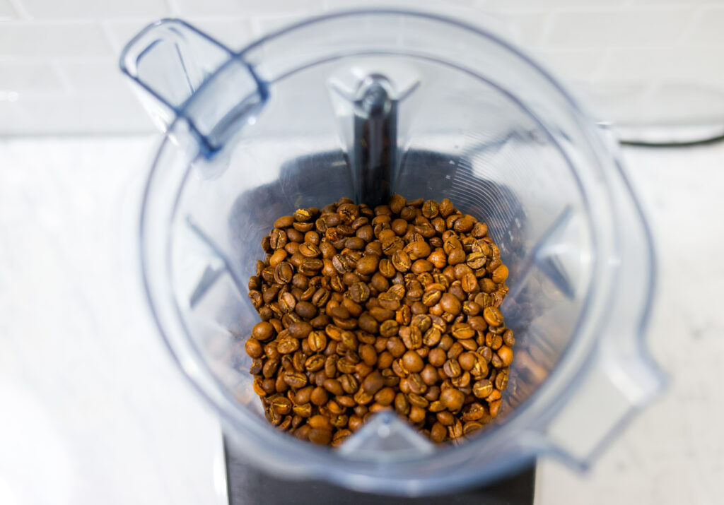 In this picture you can see the barn coffee beans in a Vitamix container. All objects are placed on white carrara marble and in the back are white metro tiles.