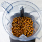 In this picture you can see the barn coffee beans in a Vitamix container. All objects are placed on white carrara marble and in the back are white metro tiles.