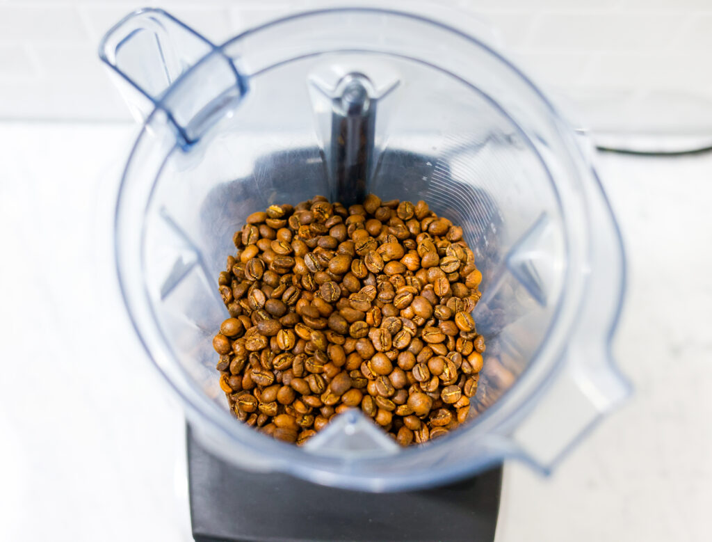 In this picture you can see the barn coffee beans in a Vitamix container. All objects are placed on white carrara marble and in the back are white metro tiles.