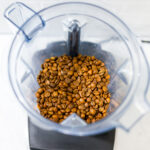 In this picture you can see the barn coffee beans in a Vitamix container. All objects are placed on white carrara marble and in the back are white metro tiles.