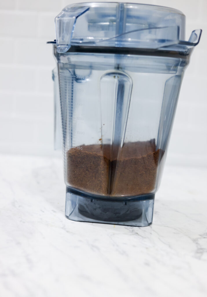 In this picture you can see the barn coffee beans grounded in a vitamix container. All objects are placed on white carrara marble and in the back are white metro tiles.