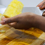 In this picture you can see a hand holding the diced pineapple spears with a knife