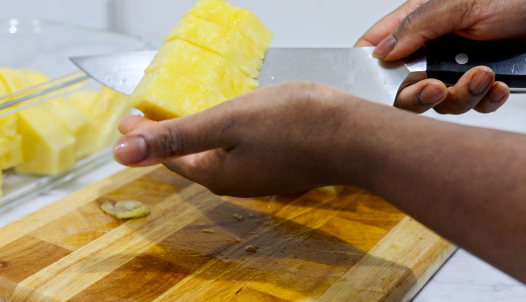 In this picture you can see a hand holding the diced pineapple spears with a knife