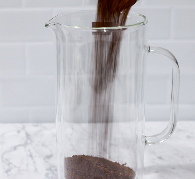 In this picture you can see a French press from the brand Zwilling filled with coarsely grounded the barn coffee beans. All objects are placed on white carrara marble and in the back are white metro tiles.